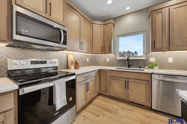 kitchen featuring appliances with stainless steel finishes, sink, backsplash, and light wood-type flooring