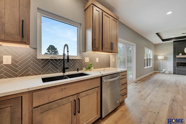 kitchen featuring sink, light wood-type flooring, stainless steel dishwasher, a fireplace, and decorative backsplash