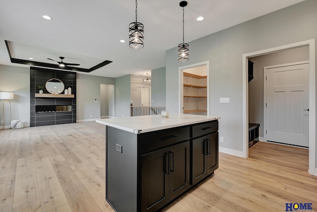 kitchen featuring light hardwood / wood-style flooring, hanging light fixtures, a center island, light stone counters, and a raised ceiling