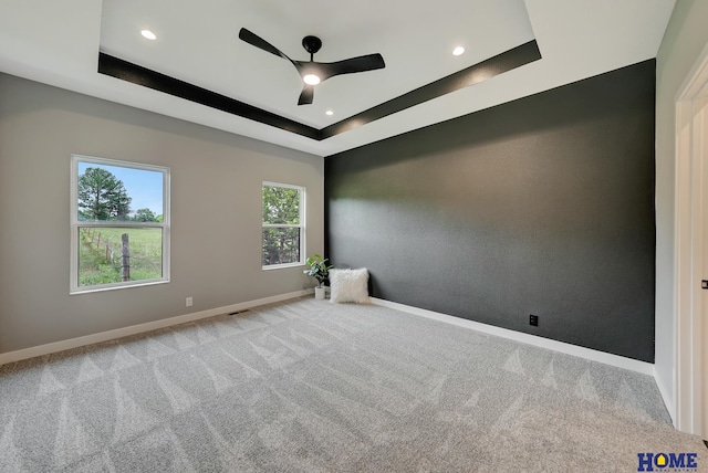 unfurnished room with a raised ceiling, light colored carpet, and ceiling fan