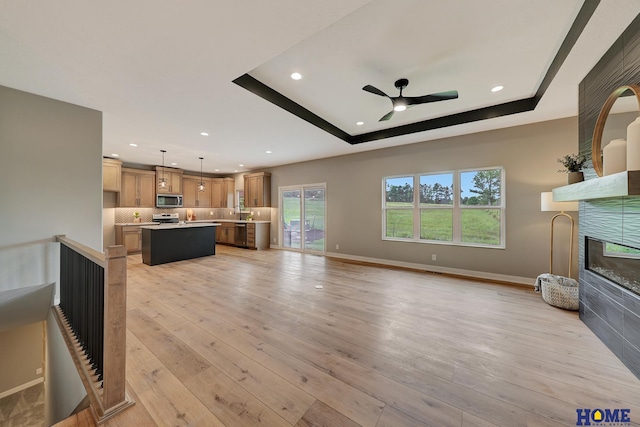 unfurnished living room featuring a tray ceiling, ceiling fan, and light wood-type flooring