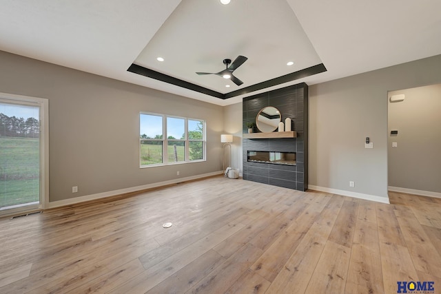 unfurnished living room with a tray ceiling, light hardwood / wood-style floors, a large fireplace, and ceiling fan