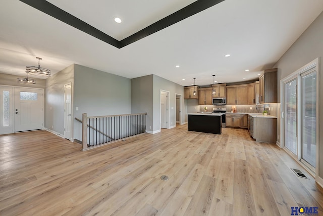 kitchen featuring tasteful backsplash, a center island, hanging light fixtures, light wood-type flooring, and stainless steel appliances