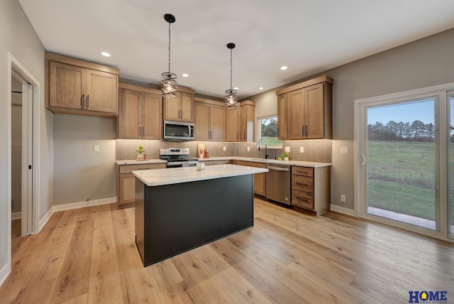 kitchen with pendant lighting, appliances with stainless steel finishes, a kitchen island, and light wood-type flooring