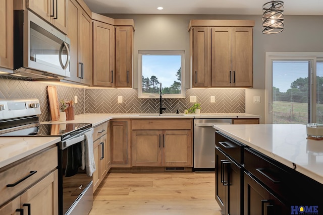 kitchen featuring sink, light stone counters, hanging light fixtures, light wood-type flooring, and stainless steel appliances