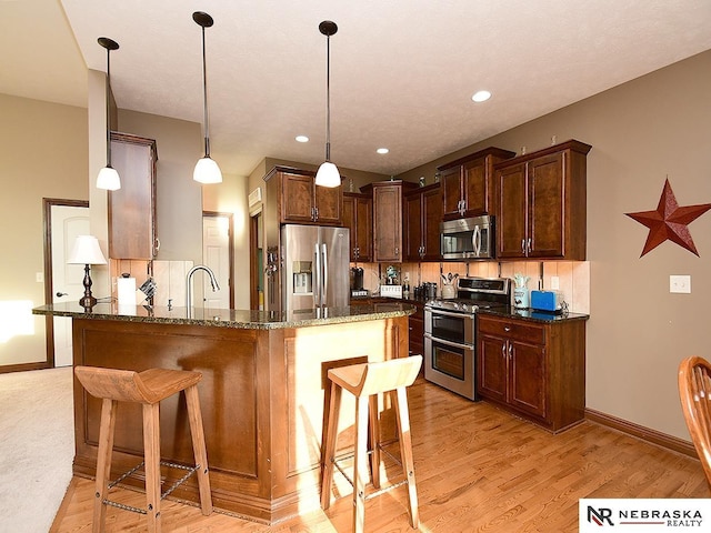 kitchen featuring stainless steel appliances, tasteful backsplash, hanging light fixtures, and dark stone countertops