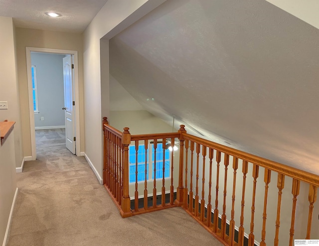 hall with vaulted ceiling, light colored carpet, and a textured ceiling