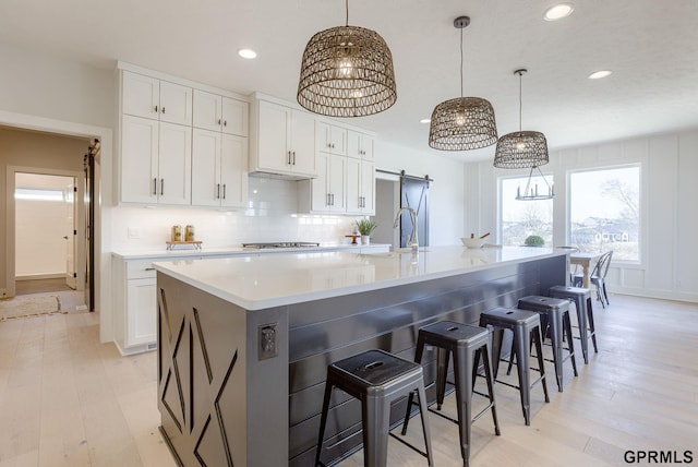 kitchen featuring white cabinets, backsplash, hanging light fixtures, a barn door, and a spacious island