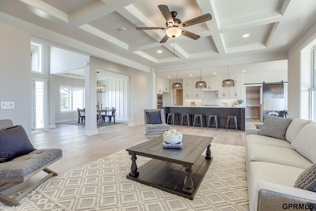 living room featuring a towering ceiling, beam ceiling, coffered ceiling, a barn door, and light wood-type flooring