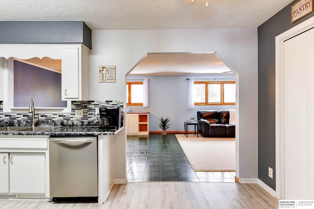 kitchen featuring white cabinets, stainless steel dishwasher, backsplash, sink, and dark stone countertops