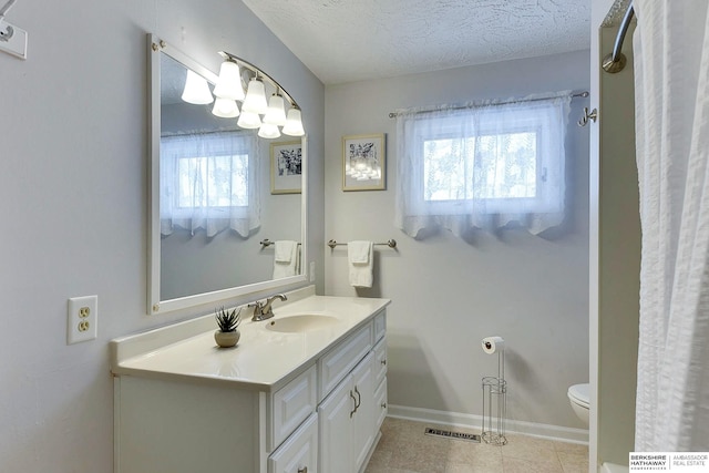 bathroom with a textured ceiling, toilet, vanity, and a wealth of natural light