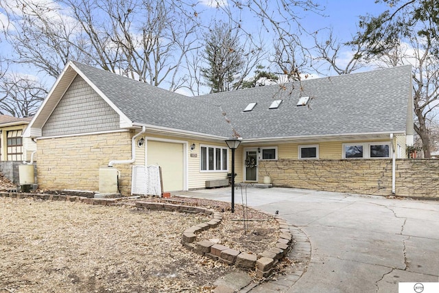 rear view of property with a garage, fence, stone siding, concrete driveway, and roof with shingles