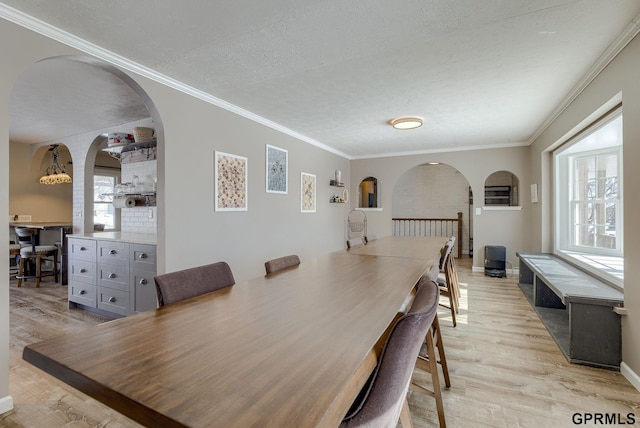 dining room with light wood-type flooring, a textured ceiling, and crown molding