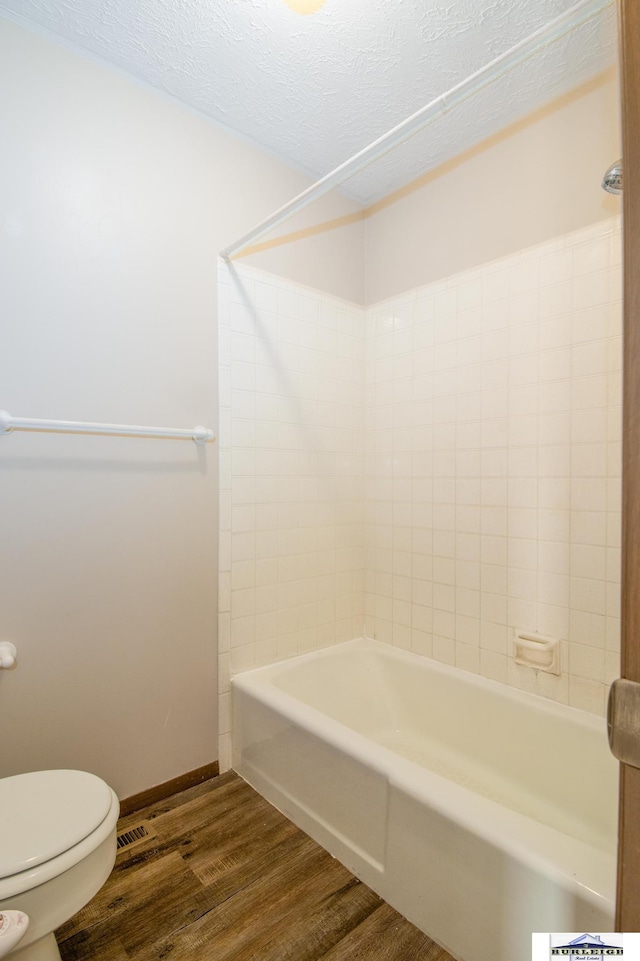 bathroom featuring tiled shower / bath, toilet, a textured ceiling, and hardwood / wood-style floors