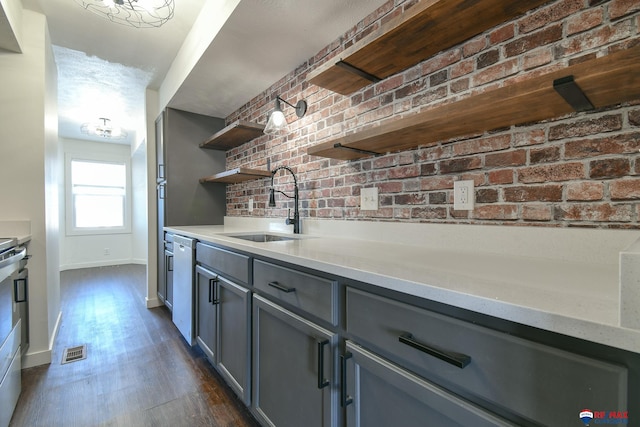 kitchen with brick wall, dark hardwood / wood-style flooring, gray cabinets, sink, and white dishwasher