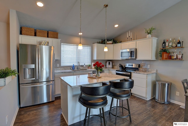 kitchen with white cabinets, lofted ceiling, a kitchen island, appliances with stainless steel finishes, and decorative light fixtures