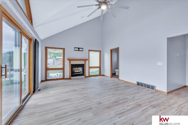 unfurnished living room featuring visible vents, a ceiling fan, light wood-style floors, a fireplace, and high vaulted ceiling