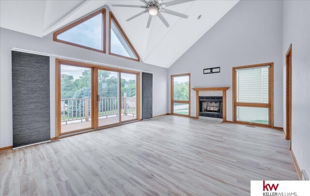 unfurnished living room with a tiled fireplace, a ceiling fan, high vaulted ceiling, light wood-type flooring, and baseboards