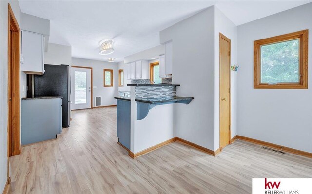 kitchen with light wood-style flooring, a peninsula, visible vents, white cabinetry, and freestanding refrigerator