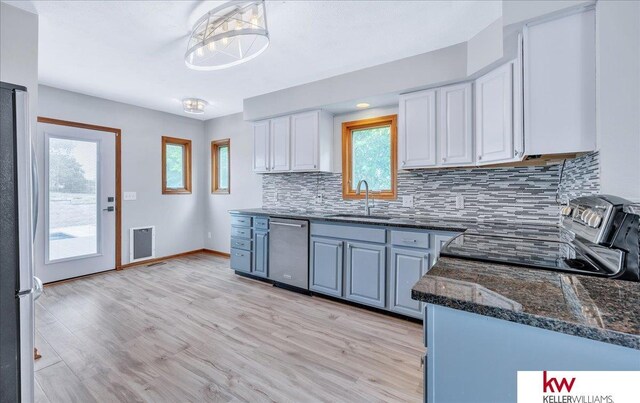 kitchen with tasteful backsplash, appliances with stainless steel finishes, white cabinets, a sink, and dark stone countertops