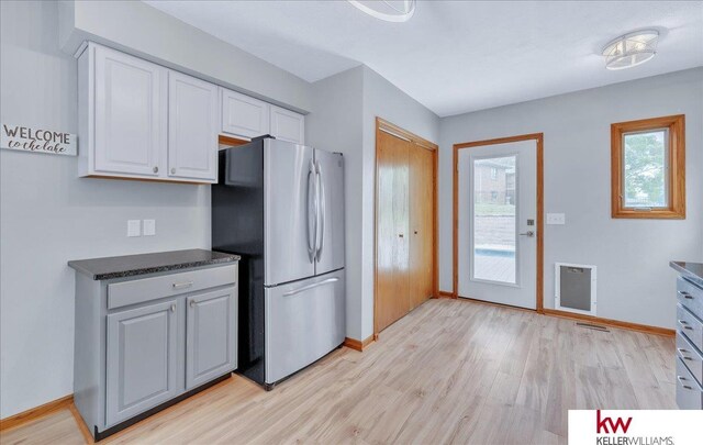 kitchen with dark countertops, light wood-style floors, freestanding refrigerator, white cabinets, and baseboards