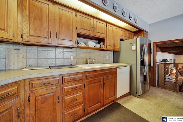 kitchen with sink, a textured ceiling, white dishwasher, stainless steel fridge, and decorative backsplash