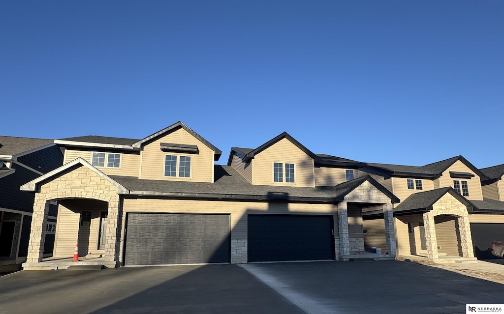 townhome / multi-family property featuring stone siding, driveway, and an attached garage