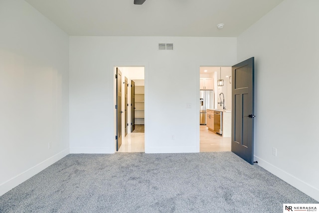 unfurnished bedroom featuring light carpet, a sink, visible vents, baseboards, and stainless steel fridge with ice dispenser