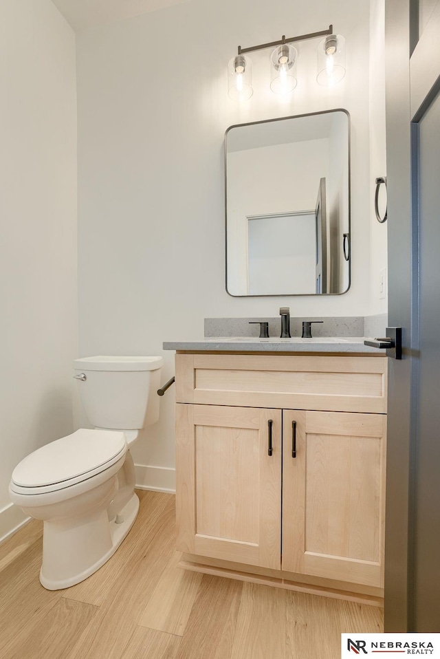 half bath featuring toilet, baseboards, wood finished floors, and vanity