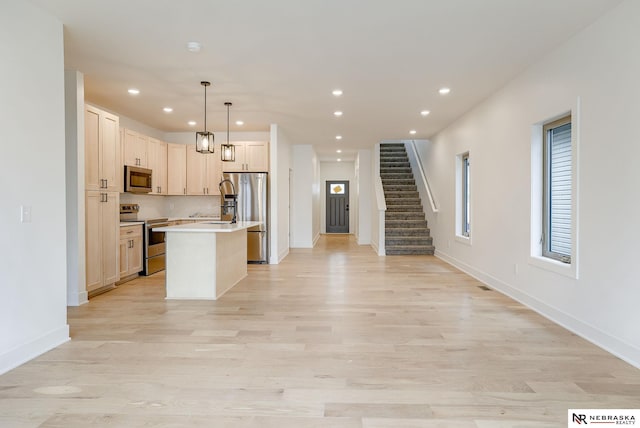 kitchen with a center island with sink, appliances with stainless steel finishes, open floor plan, light countertops, and light wood-type flooring