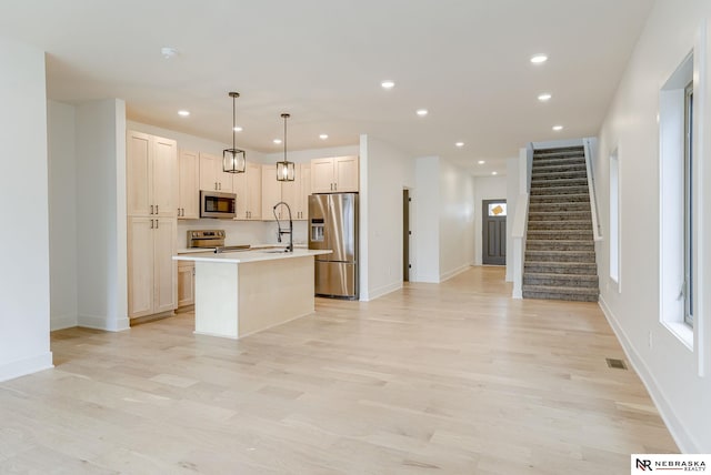 kitchen with an island with sink, appliances with stainless steel finishes, light countertops, light wood-style floors, and recessed lighting