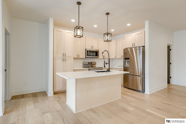 kitchen with appliances with stainless steel finishes, light countertops, a sink, and light wood finished floors