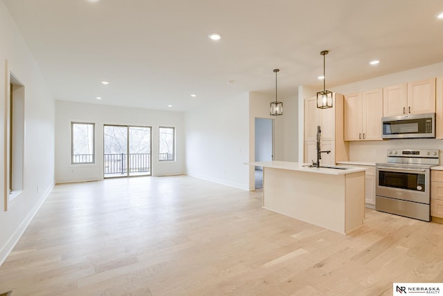 kitchen with open floor plan, a kitchen island with sink, stainless steel appliances, light countertops, and light wood-style floors