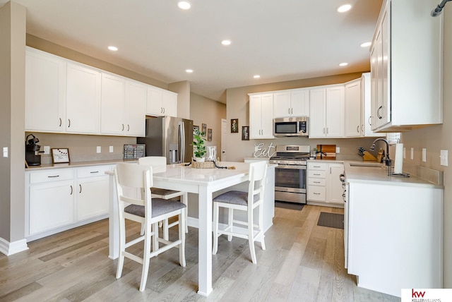 kitchen with a kitchen island, stainless steel appliances, light countertops, white cabinetry, and a sink