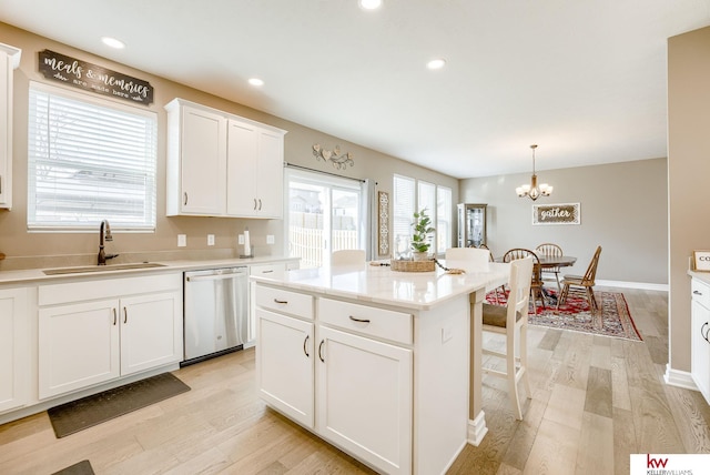 kitchen featuring a sink, light countertops, stainless steel dishwasher, hanging light fixtures, and a center island