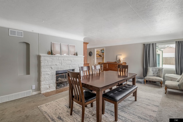 carpeted dining space featuring a stone fireplace and a textured ceiling