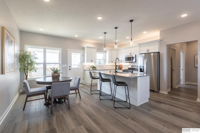 kitchen with a center island with sink, white cabinets, appliances with stainless steel finishes, dark wood-style flooring, and backsplash