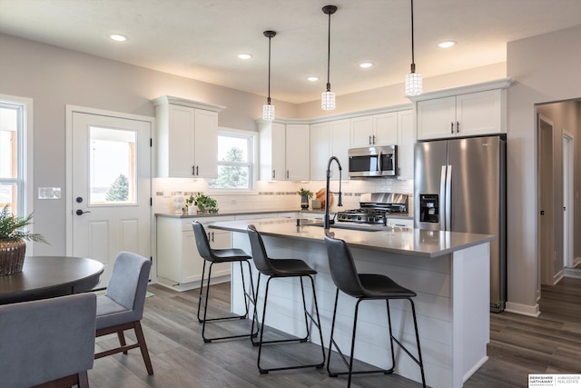 kitchen featuring a center island with sink, a breakfast bar area, backsplash, appliances with stainless steel finishes, and white cabinetry