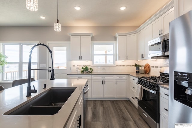 kitchen featuring hanging light fixtures, decorative backsplash, appliances with stainless steel finishes, white cabinets, and a sink