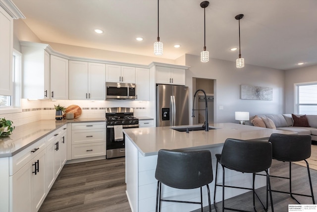 kitchen with dark wood finished floors, stainless steel appliances, backsplash, a sink, and a kitchen breakfast bar