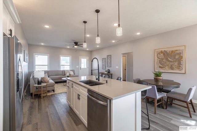 kitchen with stainless steel appliances, a sink, white cabinets, open floor plan, and a kitchen bar