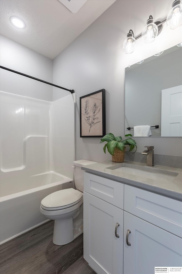 full bath featuring toilet, a textured ceiling, vanity, wood finished floors, and  shower combination