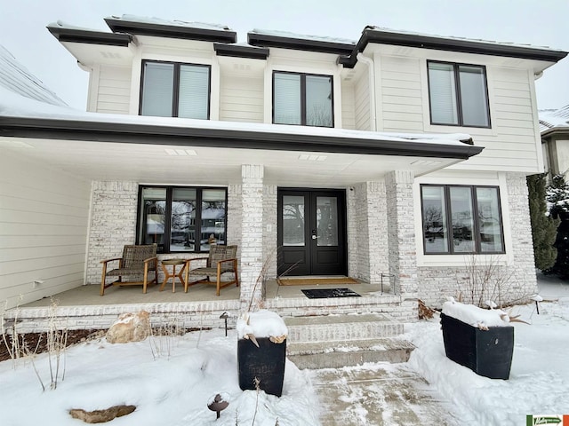 snow covered property entrance with covered porch and french doors