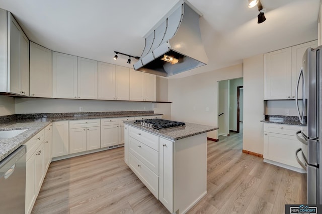 kitchen with appliances with stainless steel finishes, light hardwood / wood-style flooring, light stone counters, white cabinetry, and range hood