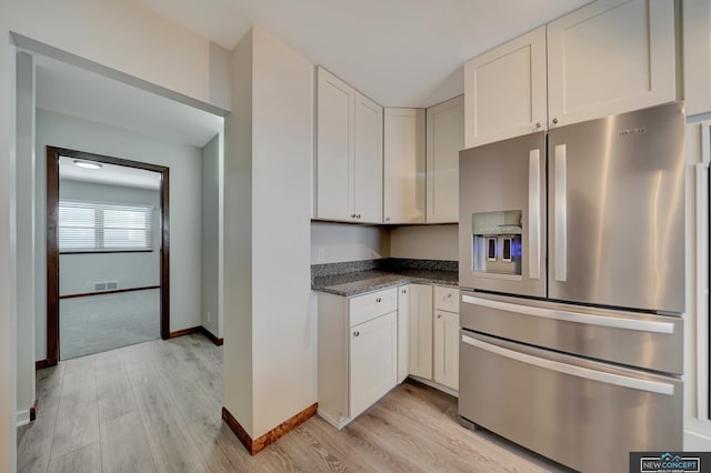 kitchen with light hardwood / wood-style flooring, white cabinetry, dark stone countertops, and stainless steel fridge