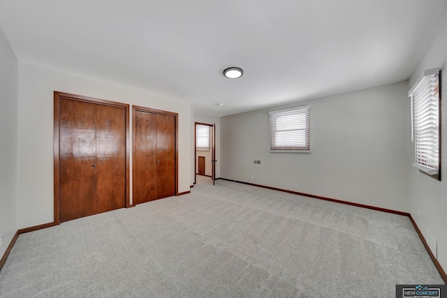 unfurnished bedroom featuring light carpet and two closets