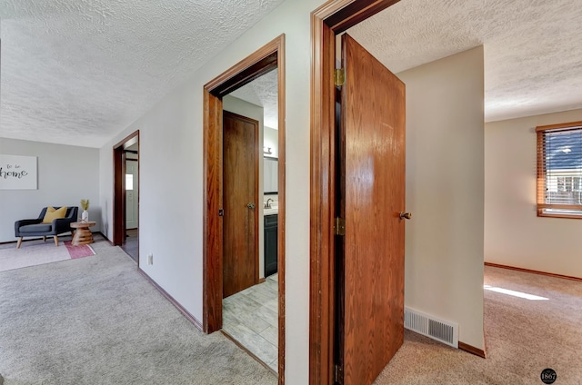 hall featuring a textured ceiling, carpet floors, visible vents, and baseboards