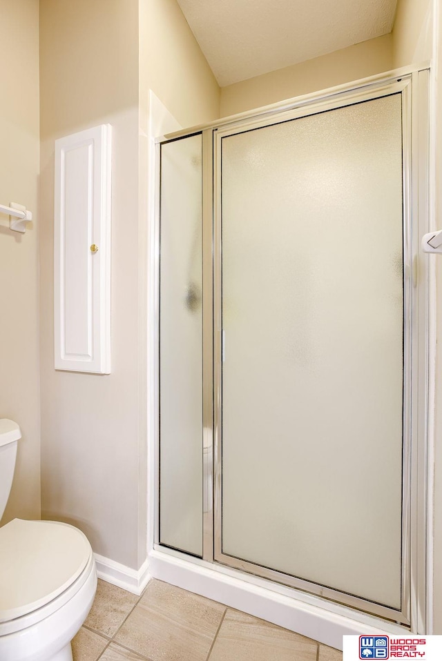 bathroom featuring tile patterned floors, toilet, and a shower with shower door