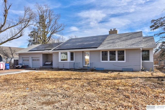 ranch-style house with a garage, roof mounted solar panels, a chimney, and concrete driveway