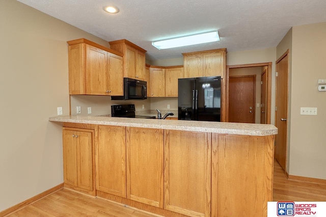 kitchen featuring light hardwood / wood-style floors, kitchen peninsula, a textured ceiling, and black appliances